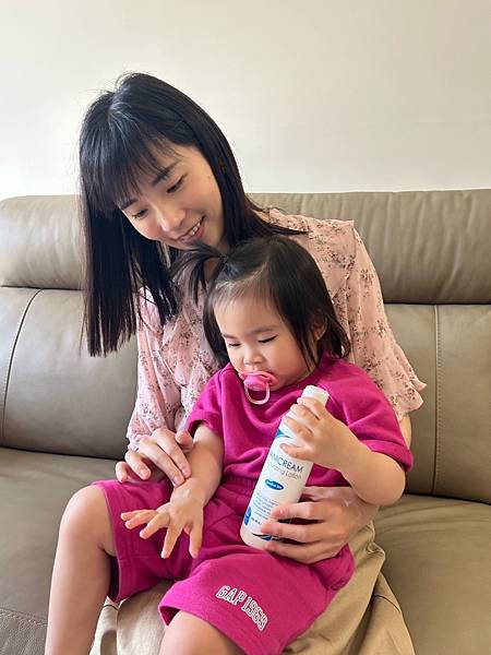 由坎蒂絲冒險日誌拍攝抱著女兒坐在沙發上手拿著無油安膚清爽調理乳液
