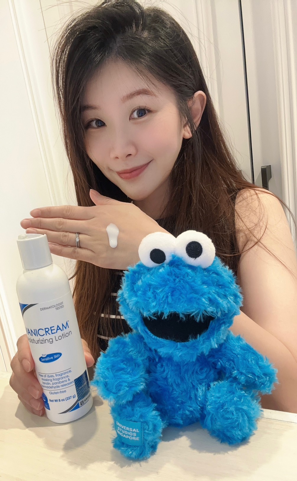 薇琪の萬得窩拍攝vicky坐在米色的桌面前將薇霓肌本無油安膚清爽調理乳液擠在左手背上，周圍有一隻Cookie Monster娃娃