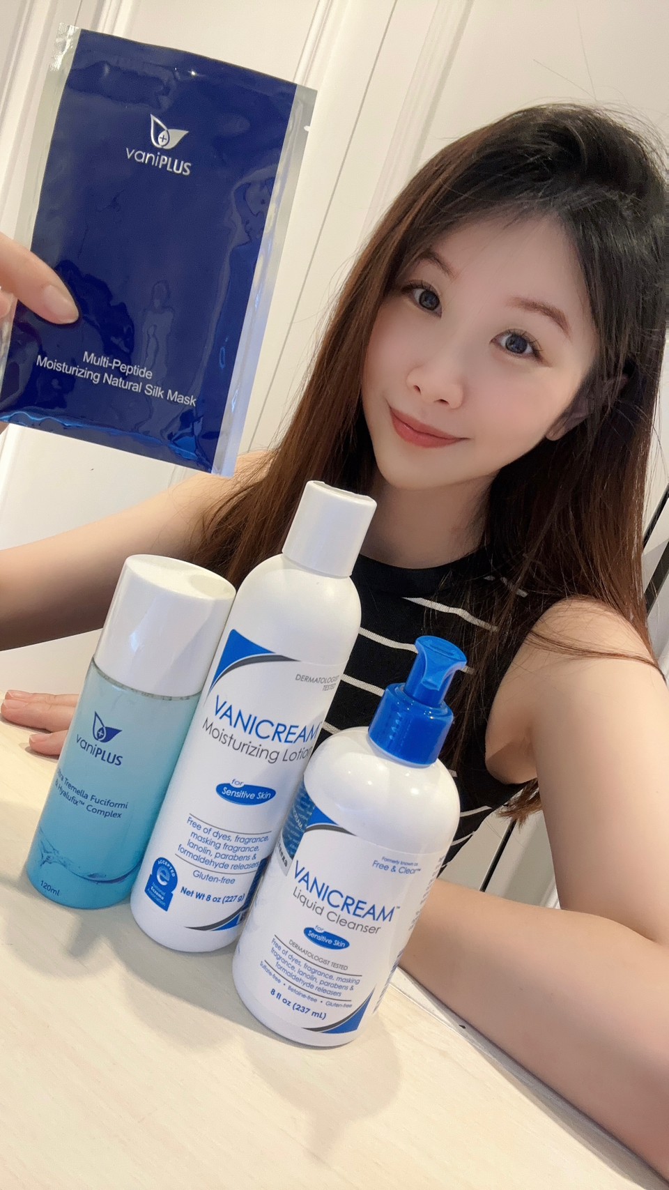 薇琪の萬得窩拍攝vicky在米色的桌面前手上拿著一片薇霓進階三效安瓶絲膜與產品拍合照，包含薇霓肌本胺基酸調理潔膚露、薇霓肌本無油安膚清爽調理乳液、薇霓進階極潤雪耳精露