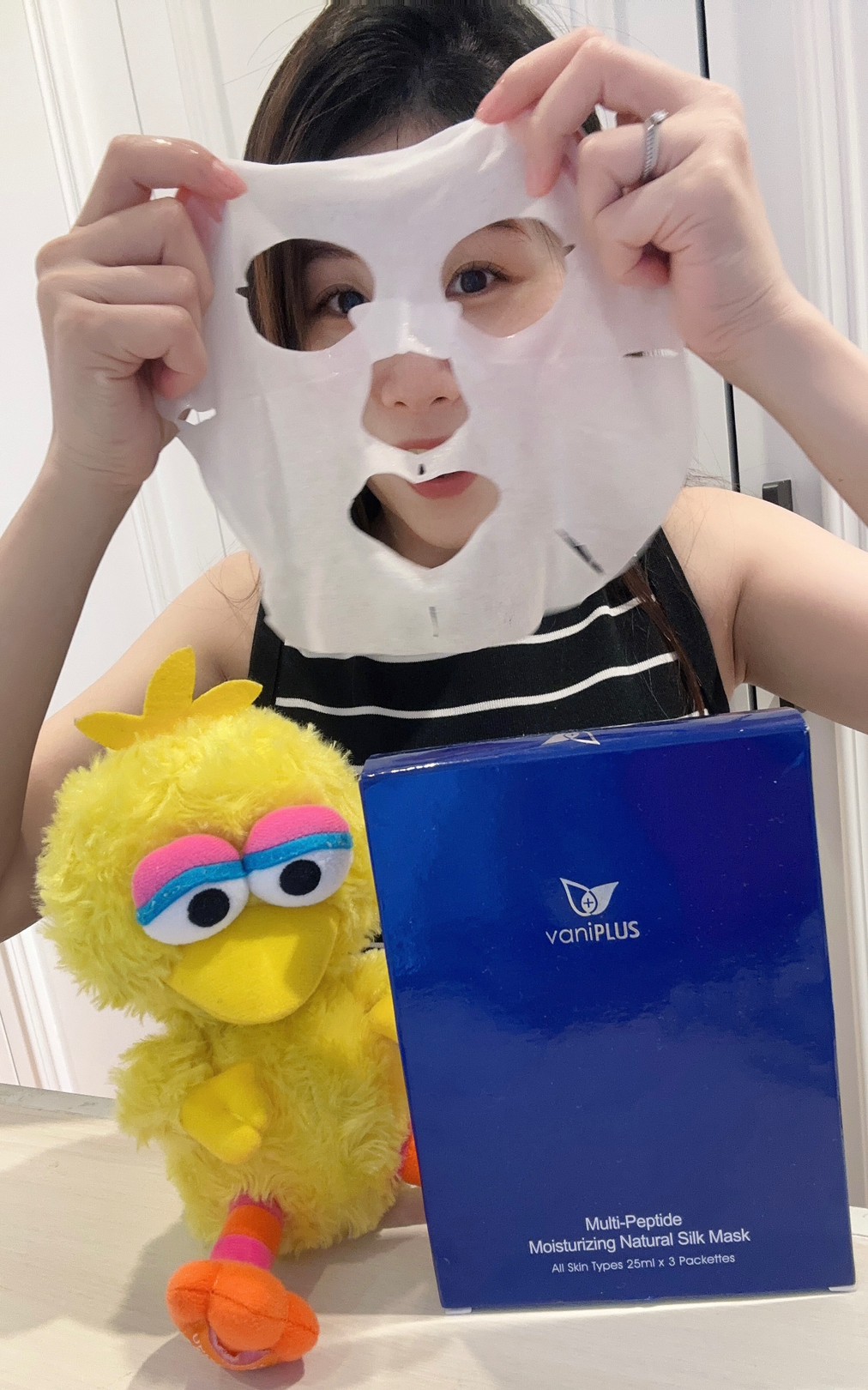 薇琪の萬得窩拍攝vicky將特選類蠶絲布製成的薇霓進階三效安瓶絲膜拿起，準備敷在臉上，周圍有一隻Big Bird娃娃