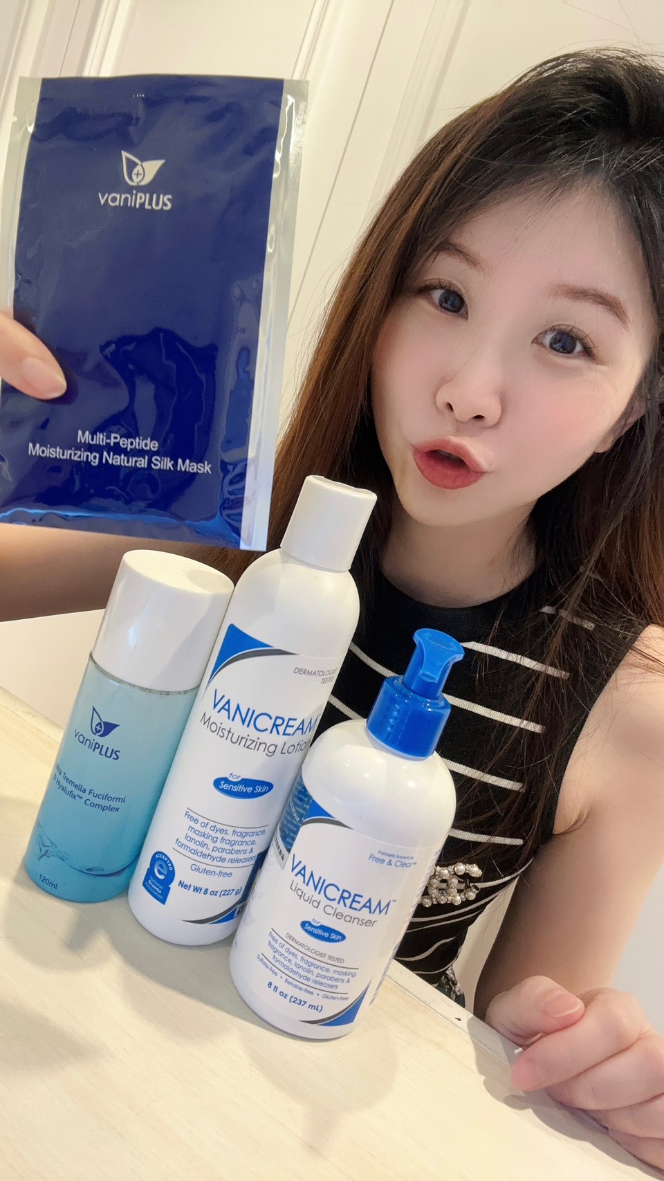 薇琪の萬得窩拍攝vicky手上拿著一片薇霓進階三效安瓶絲膜在米色的桌面上與產品拍合照，包含薇霓肌本胺基酸調理潔膚露、薇霓肌本無油安膚清爽調理乳液、薇霓進階極潤雪耳精露