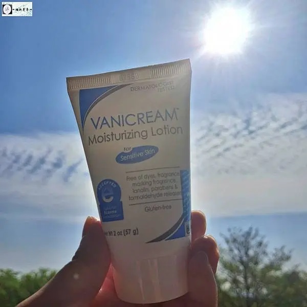 一隻手輕輕握著薇霓肌本無油安膚清爽調理乳液旅行瓶。背景為藍天白雲，陽光透過雲層照射下來，營造出一種清新、自然的氛圍