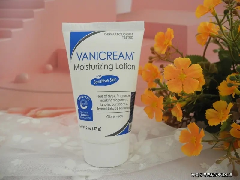 這張照片展示了VANICREAM薇霓肌本無油安膚清爽調理乳液旅行瓶的產品照，包裝上標示了美國濕疹協會認證，淺粉色背景，帶有淺色紋路，以及一些橘色花朵裝飾。