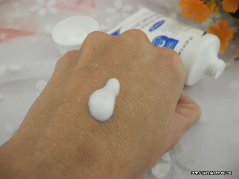 這張照片展示了VANICREAM薇霓肌本無油安膚清爽調理乳液旅行瓶的產品照，以及一隻手和一些橘色花朵，手背上擠出少量白色乳霜，展示產品的質地。