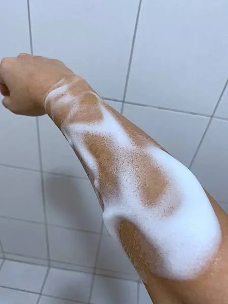 照片以近距離拍攝，將焦點完全集中在手臂上的vaniPLUS天然燕麥潔膚慕斯泡沫狀。清晰的光線照射在手臂上，呈現出泡沫的質感和皮膚的紋理。