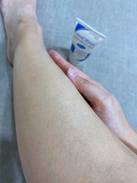照片以俯視的角度拍攝，將腿部、手和VANICREAM薇霓肌本無油安膚清爽調理乳液旅行瓶軟管作為主要焦點。手握住腿部的動作，以及旁邊放置的乳液，暗示了這款乳液被用於腿部的保濕護理。