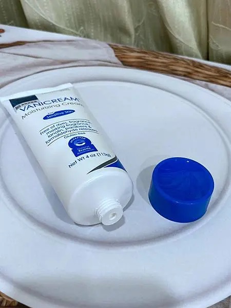 照片以俯視的角度展示了VANICREAM薇霓肌本全日高效修護保濕乳霜和它的瓶蓋，白色的盤子和淺色的背景使產品本身更加突出。整體的燈光自然，呈現出一種日常使用的情景。
