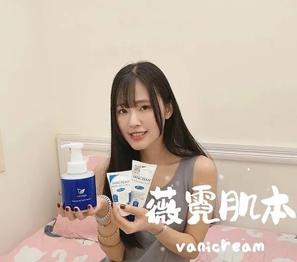 一位年輕女性，留著深色長髮和齊瀏海，化著淡妝，室內環境，一張鋪著粉色和白色床單的床，以及白色的床頭板和牆壁。照片的右側疊加了白色的中文字薇霓肌本和英文字vanicream。