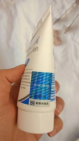 這張照片展示了一隻手握著一條VANICREAM薇霓肌本無油安膚清爽調理乳液旅行瓶的底部，特別突顯了防偽標籤。