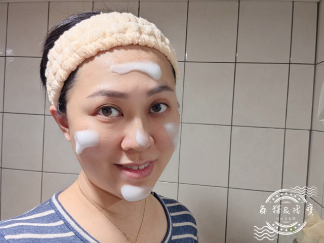 女性將薇霓進階天然燕麥潔膚慕斯泡沫點塗於臉部五處，包含額頭、雙頰、鼻頭與下巴，背景為浴室磁磚，呈現潔膚實際使用情境