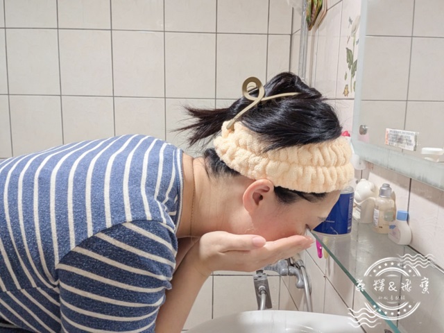女性在浴室使用薇霓進階天然燕麥潔膚慕斯洗臉後低頭用清水沖洗泡沫，雙手掬水洗臉，背景為洗面台與鏡櫃