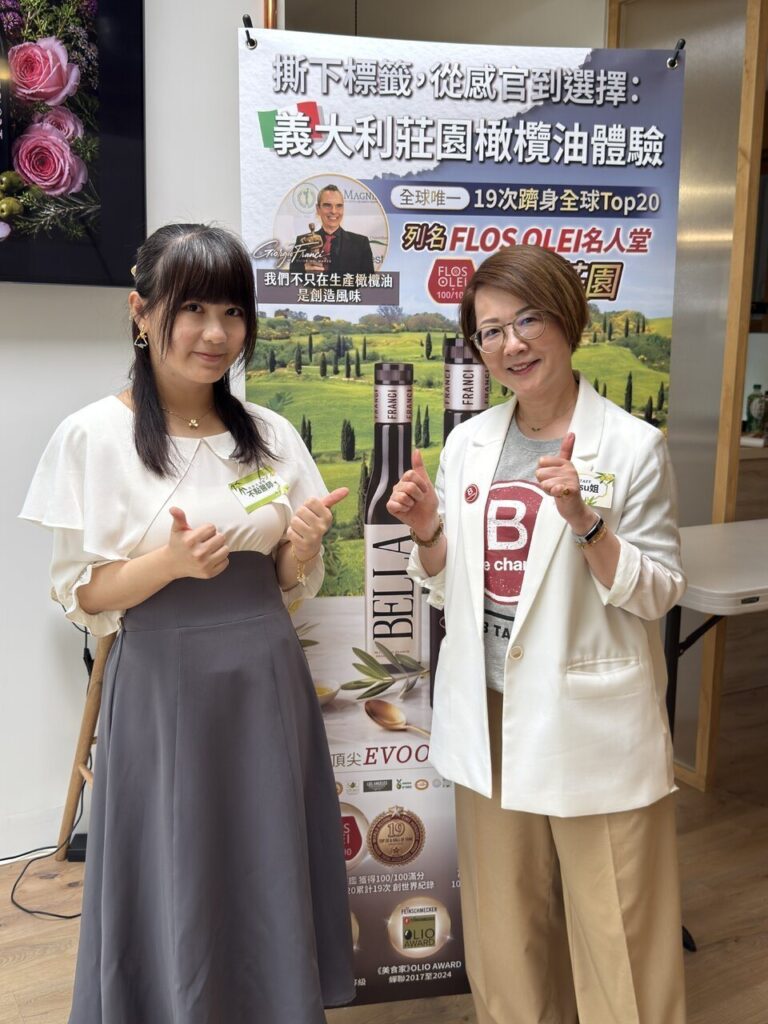 照片3 義大利莊園橄欖油體驗活動現場。兩位女性在活動宣傳海報前雙手比讚合影。後方海報印有「撕下標籤,從感官到選擇:義大利莊園橄欖油體驗」、「列名 FLOS OLEI 名人堂」等文字,並展示 FRANCI 的 BELLA 橄欖油瓶身與莊園風景。