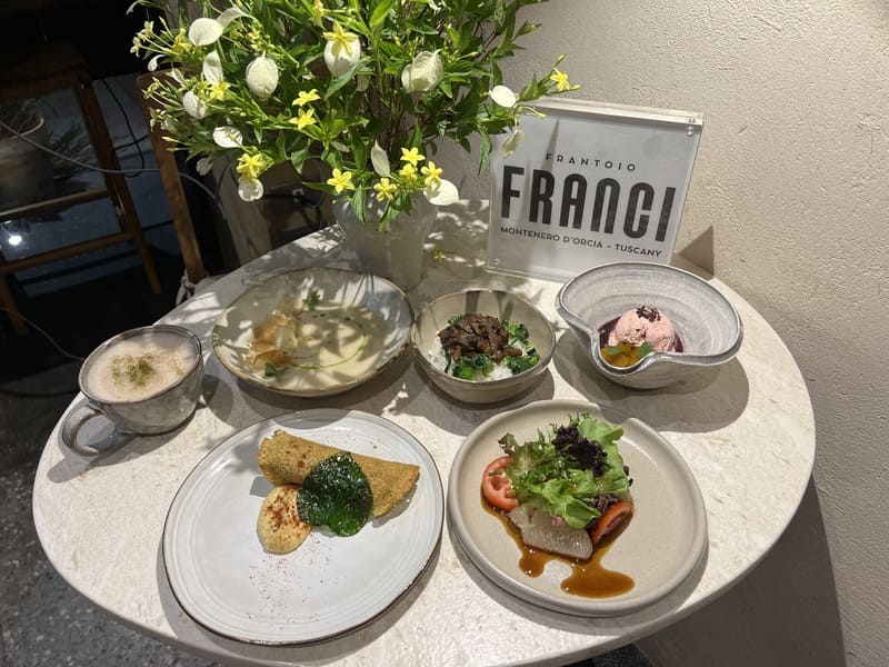 義大利Frantoio Franci精品特級初榨橄欖油全植蔬食饗宴。圓桌陳列品牌立牌與花藝,搭配酥脆捲餅、生菜沙拉、濃湯、滷肉飯與冰淇淋等料理,展現頂級莊園油佐餐搭配。