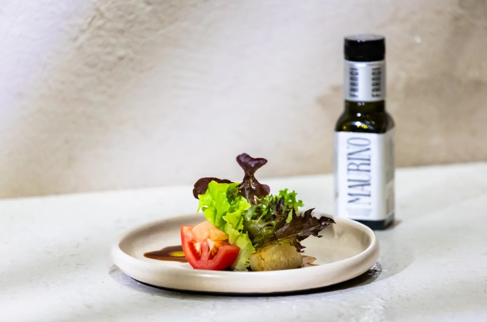 義大利Franci特級初榨橄欖油料理圖。淺色陶瓷盤盛裝番茄切片、生菜沙拉與油醋醬汁,右後方展示Franci Maurino橄欖油黑瓶,展現地中海蔬食美饌與精緻餐桌氛圍。
